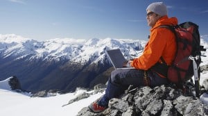 A man uses his laptop on a mountain top